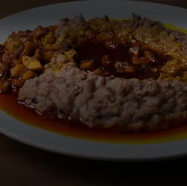 Beans topped with a dark pepper sauce on a white plate