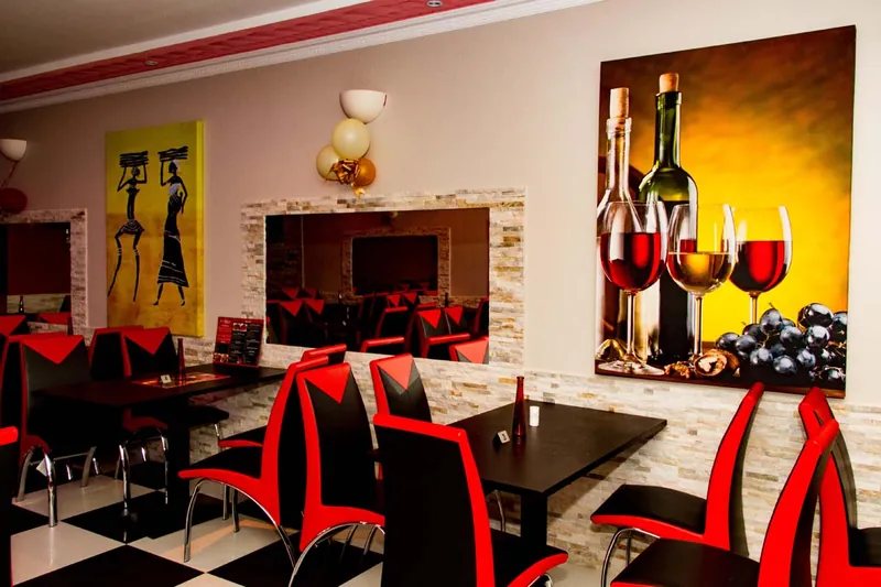 Tables and red and black chairs below a painting of wine bottles and glasses
