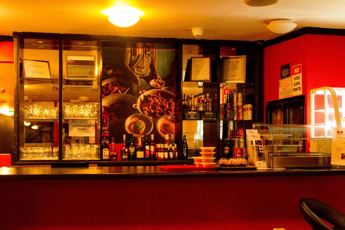 The bar counter, with glasses and bottles on the shelves behind it