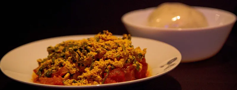 Egusi on a plate with a bowl of pounded yam behind it