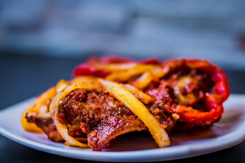 Peppered meat with strips of red and yellow pepper on a white plate